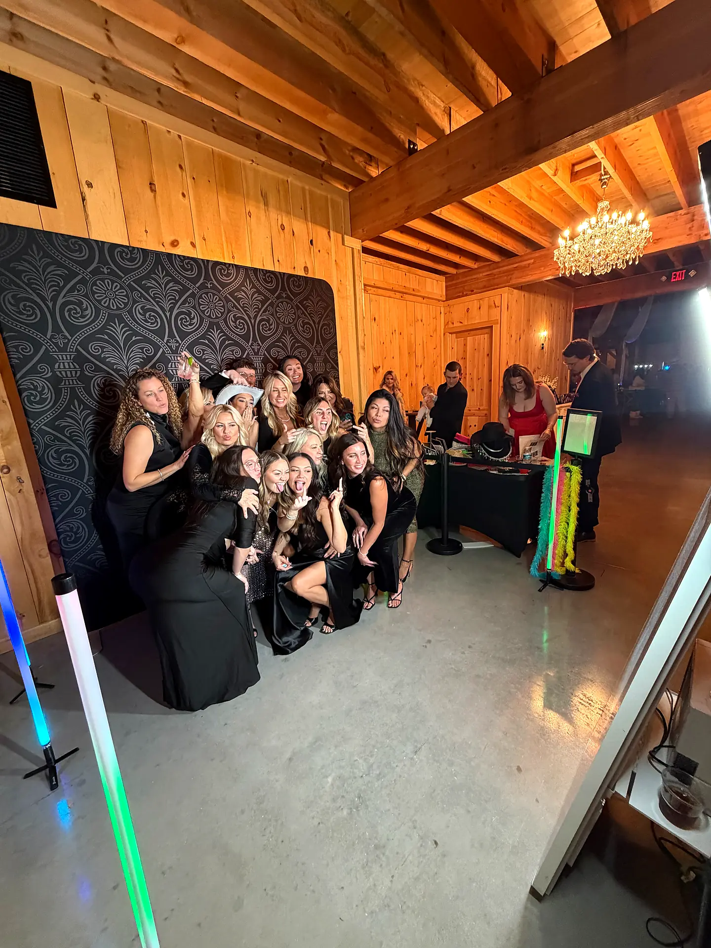 Group of guests poses together in front of a black damask backdrop at a Big Events photo booth inside a barn venue in Alva
