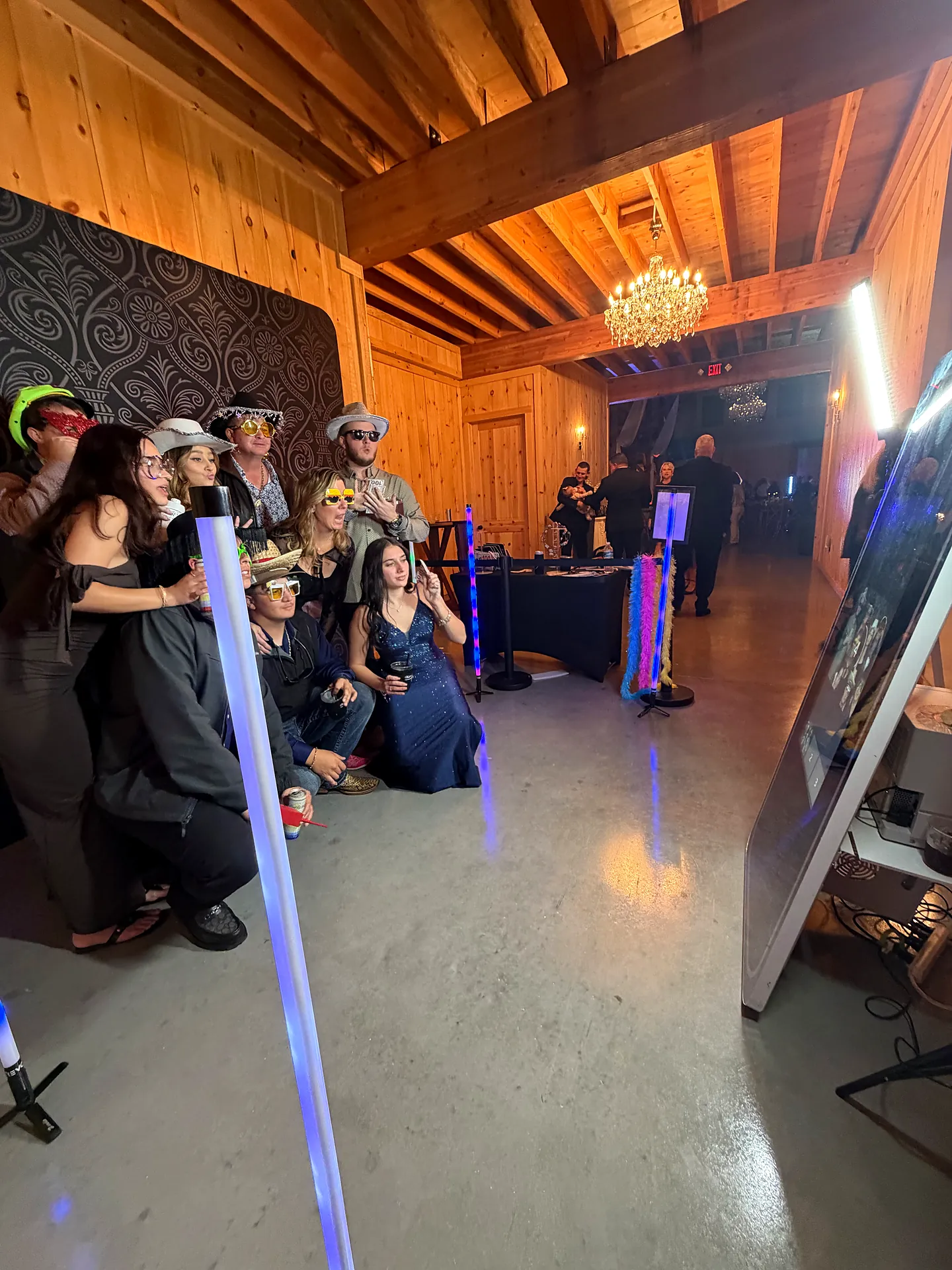 Guests in cowboy hats and party glasses pose with props at a photo booth in a rustic barn venue in Alva