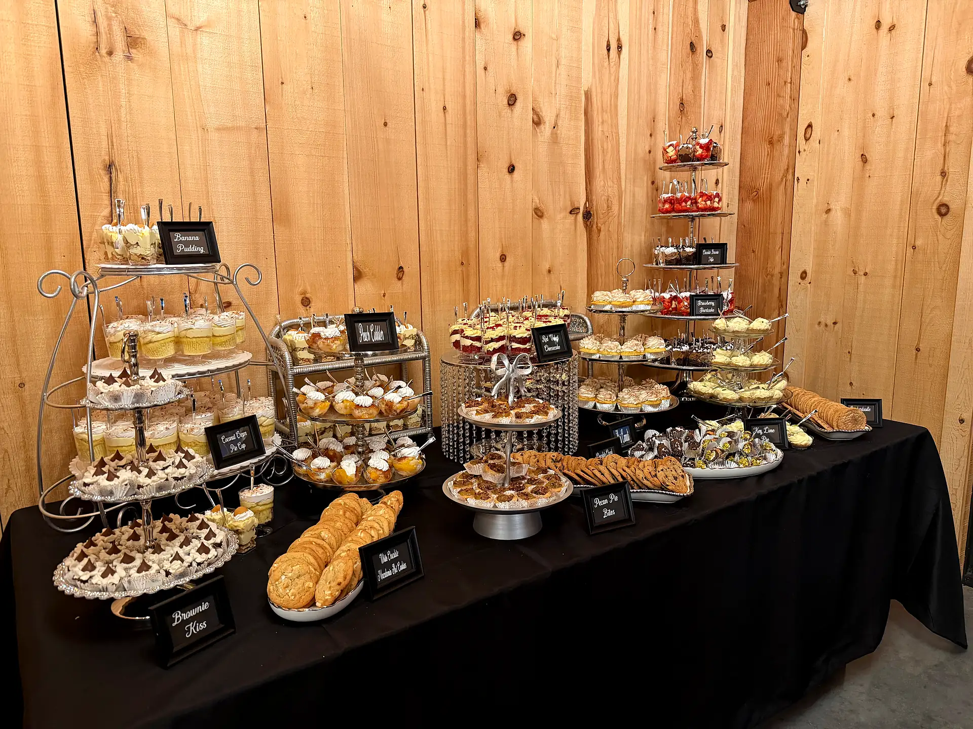 Elegant dessert table with tiered stands of mini desserts and cookies at a rustic barn venue in Alva