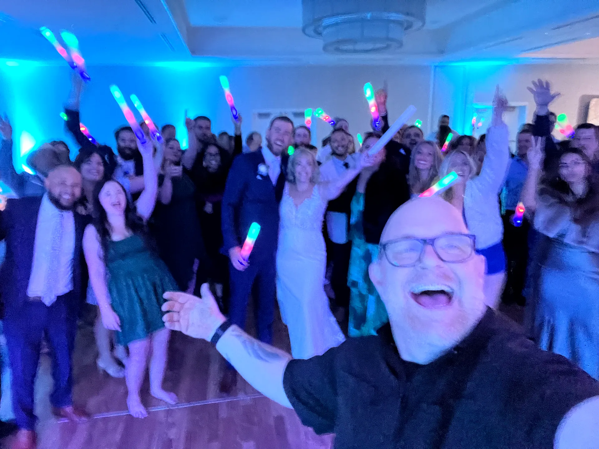 DJ Bigs celebrates with a packed dance floor of wedding guests holding glow sticks in Fort Myers Beach
