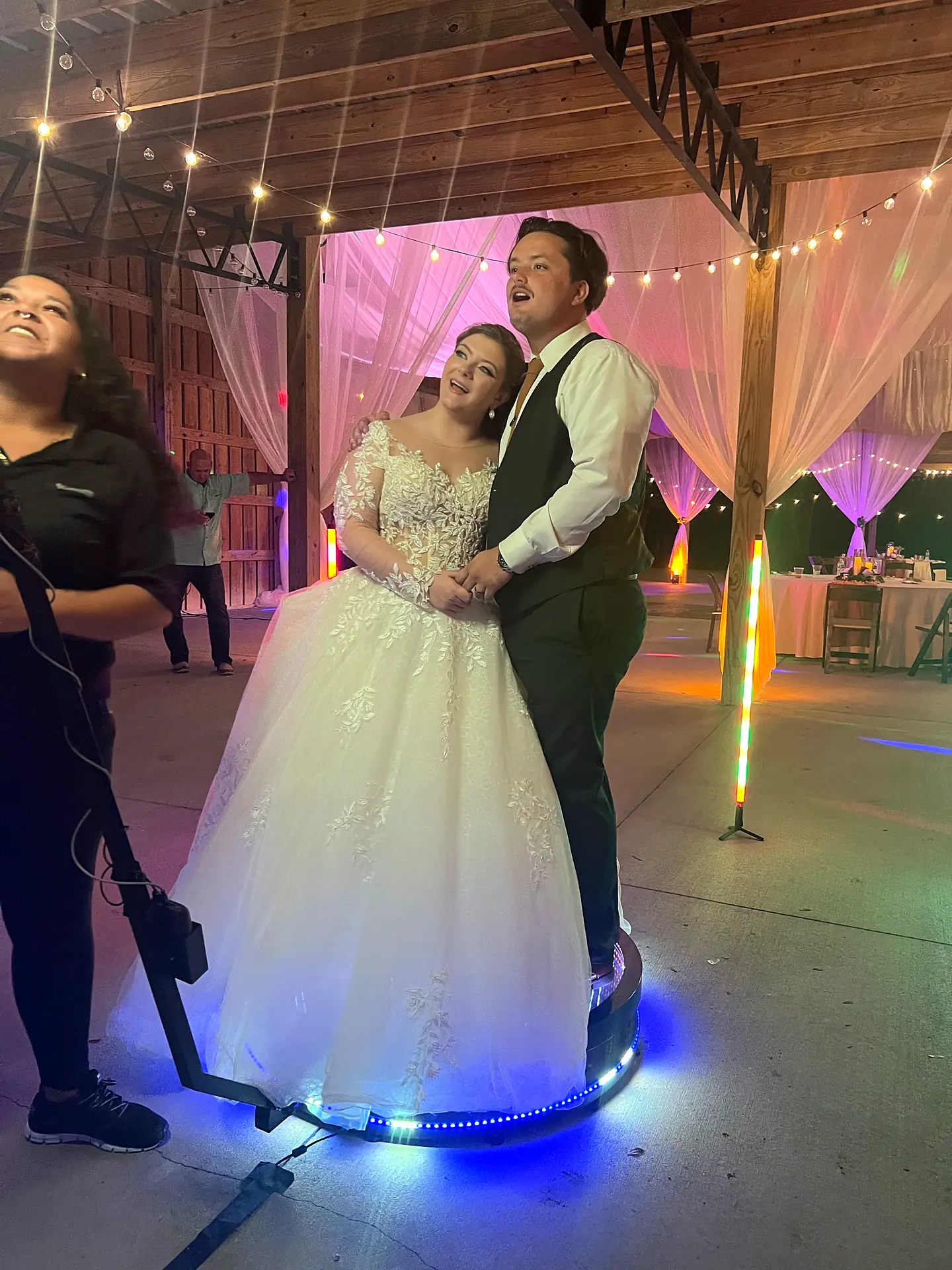 Bride and groom ride an LED 360 photo booth platform with help from a Big Events attendant at a rustic wedding near LaBelle