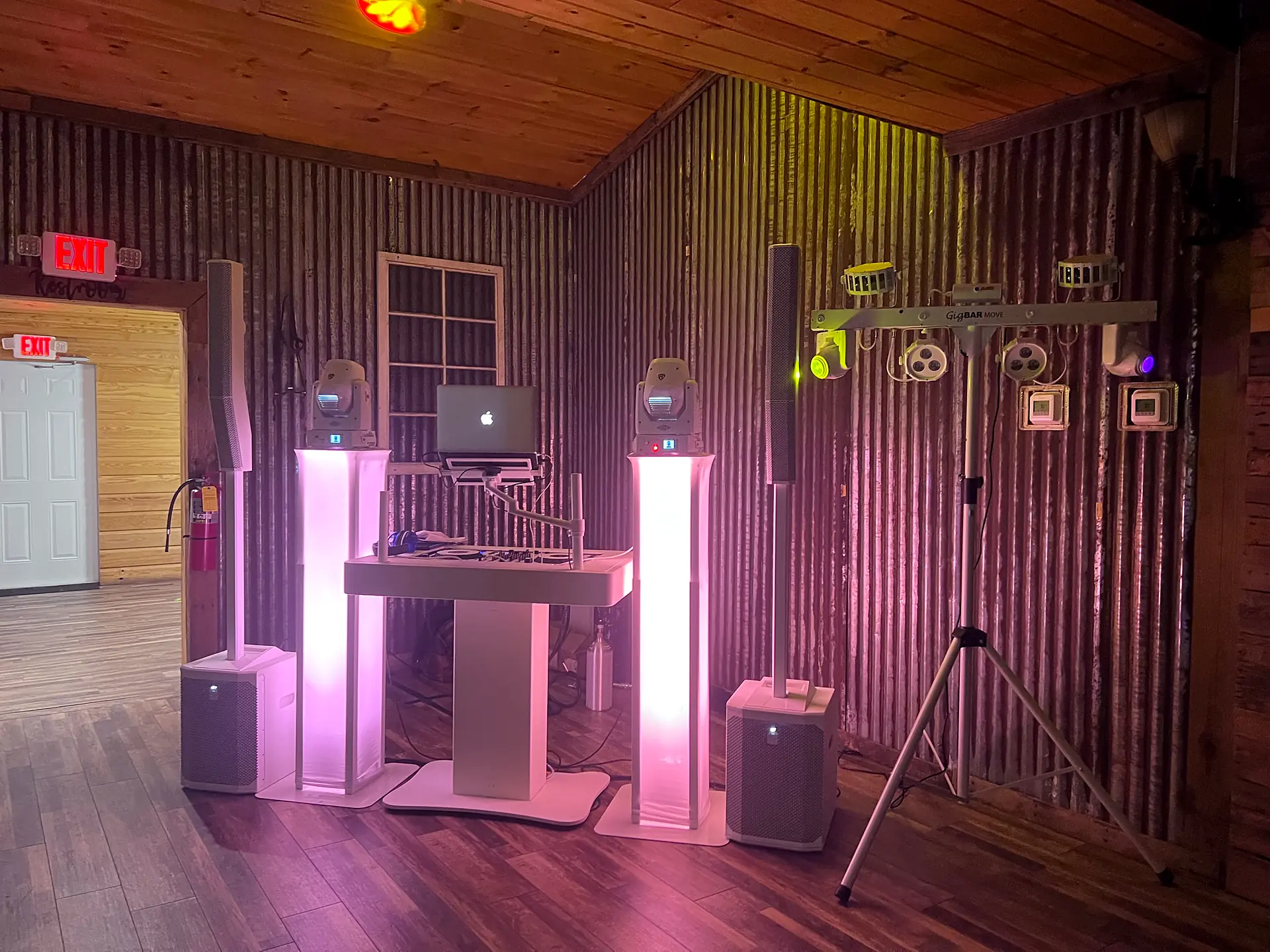 Wedding DJ booth with glowing totems, moving-head lights and speakers set up in a rustic wood venue in the Naples area