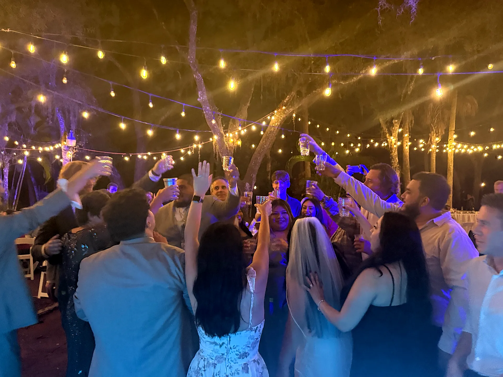 Bride and guests raise a toast under string lights and oak trees at an outdoor wedding reception in North Fort Myers