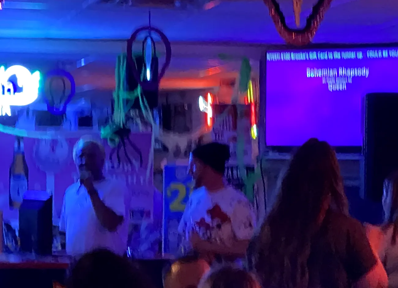 A karaoke singer on the mic beside the lyrics screen at a packed Southwest Florida bar on a Big Events Florida karaoke night