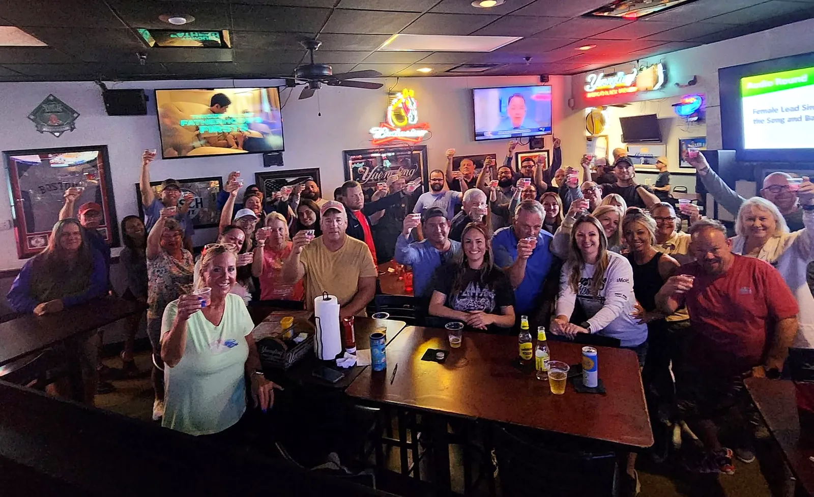 About 40 trivia players raise their glasses for the camera during the audio round of a packed sports bar trivia night in Southwest Florida