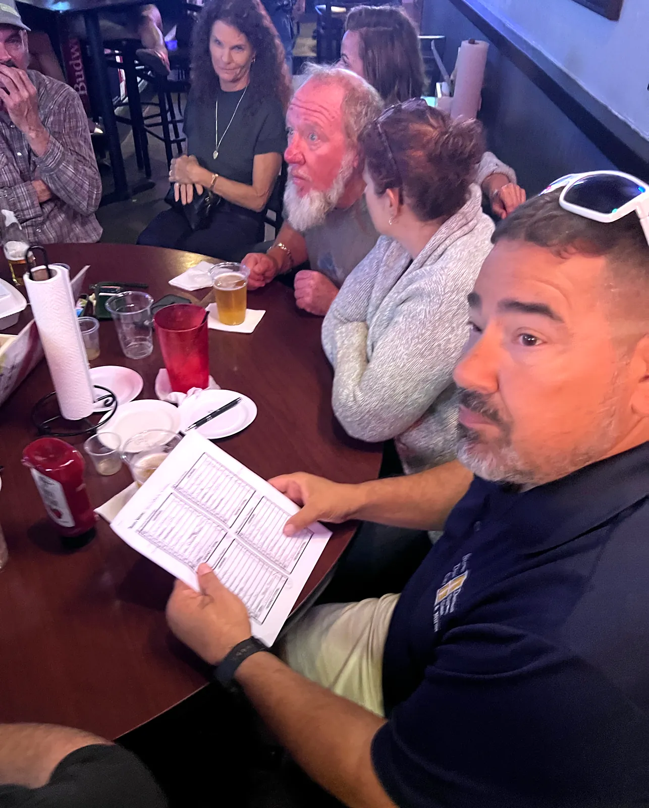 A trivia team gathers around a table as one player holds their answer sheet at a Southwest Florida bar trivia night